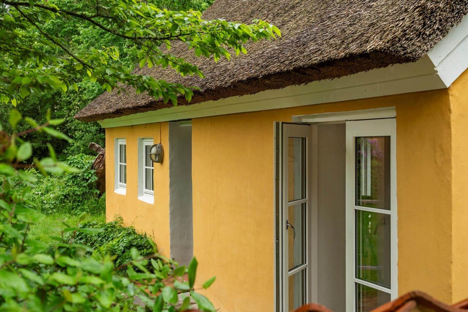 A yellow house with thatched roof and open door in the green.