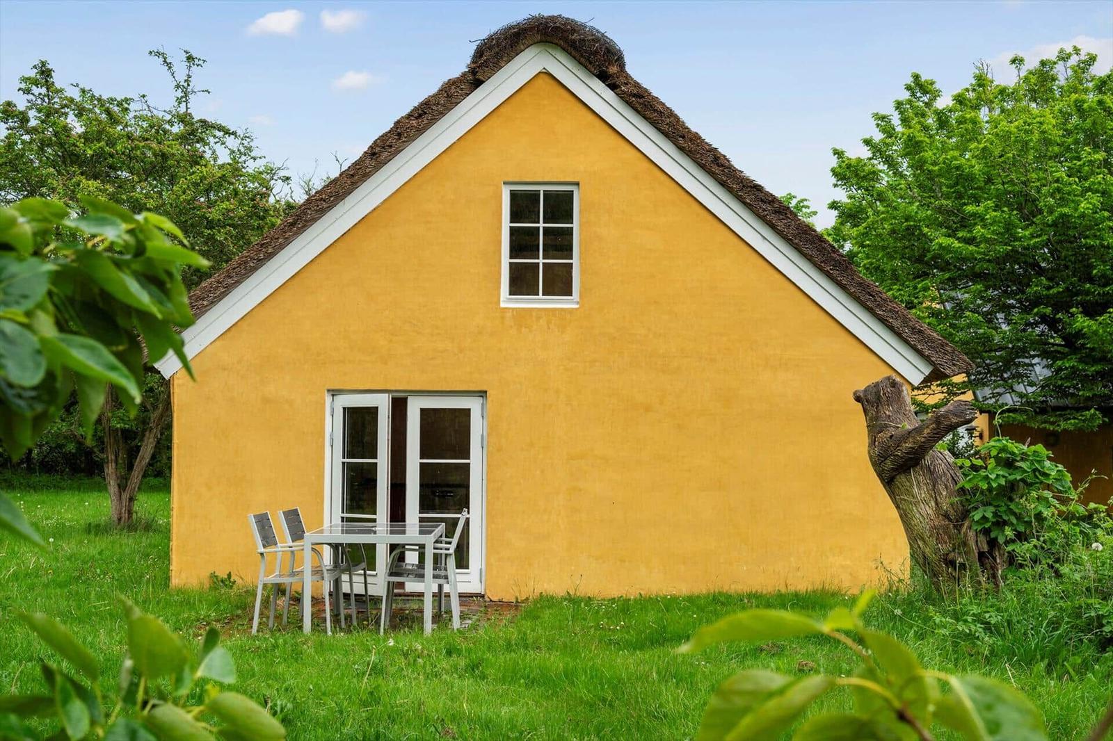 A yellow house with thatched roof, window, and terrace with table and chairs.