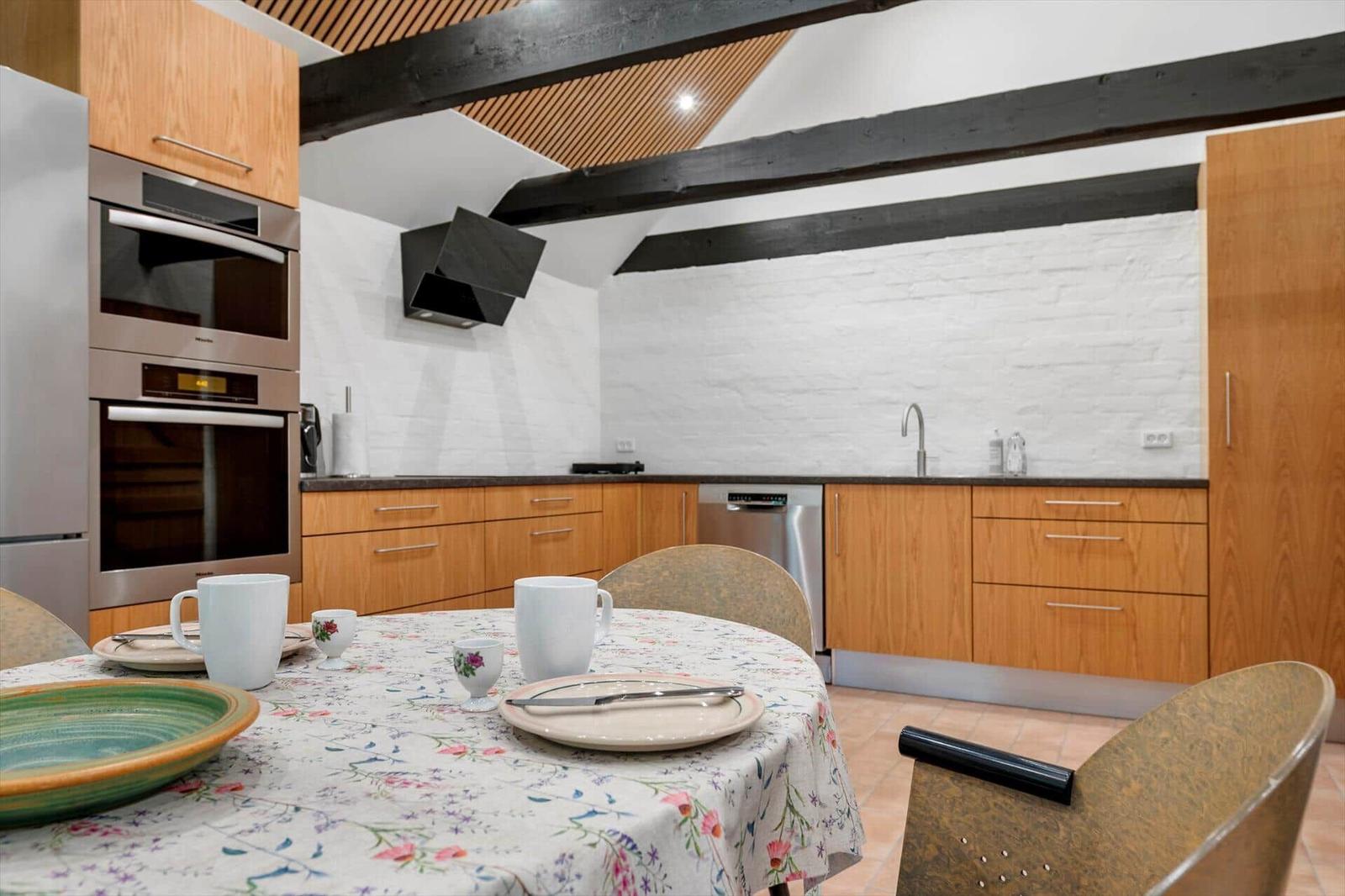 Kitchen with dining area, wooden cabinets, white wall and black beams.