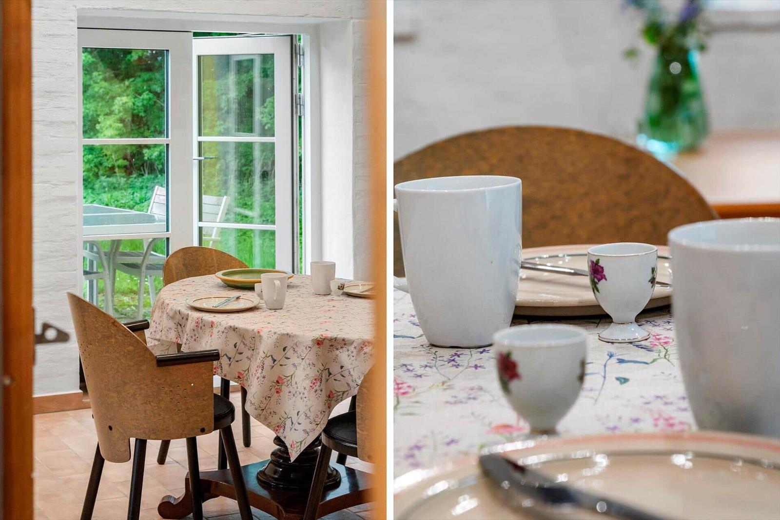 Dining table with tablecloth and chairs. Passage to terrace with view of green areas.