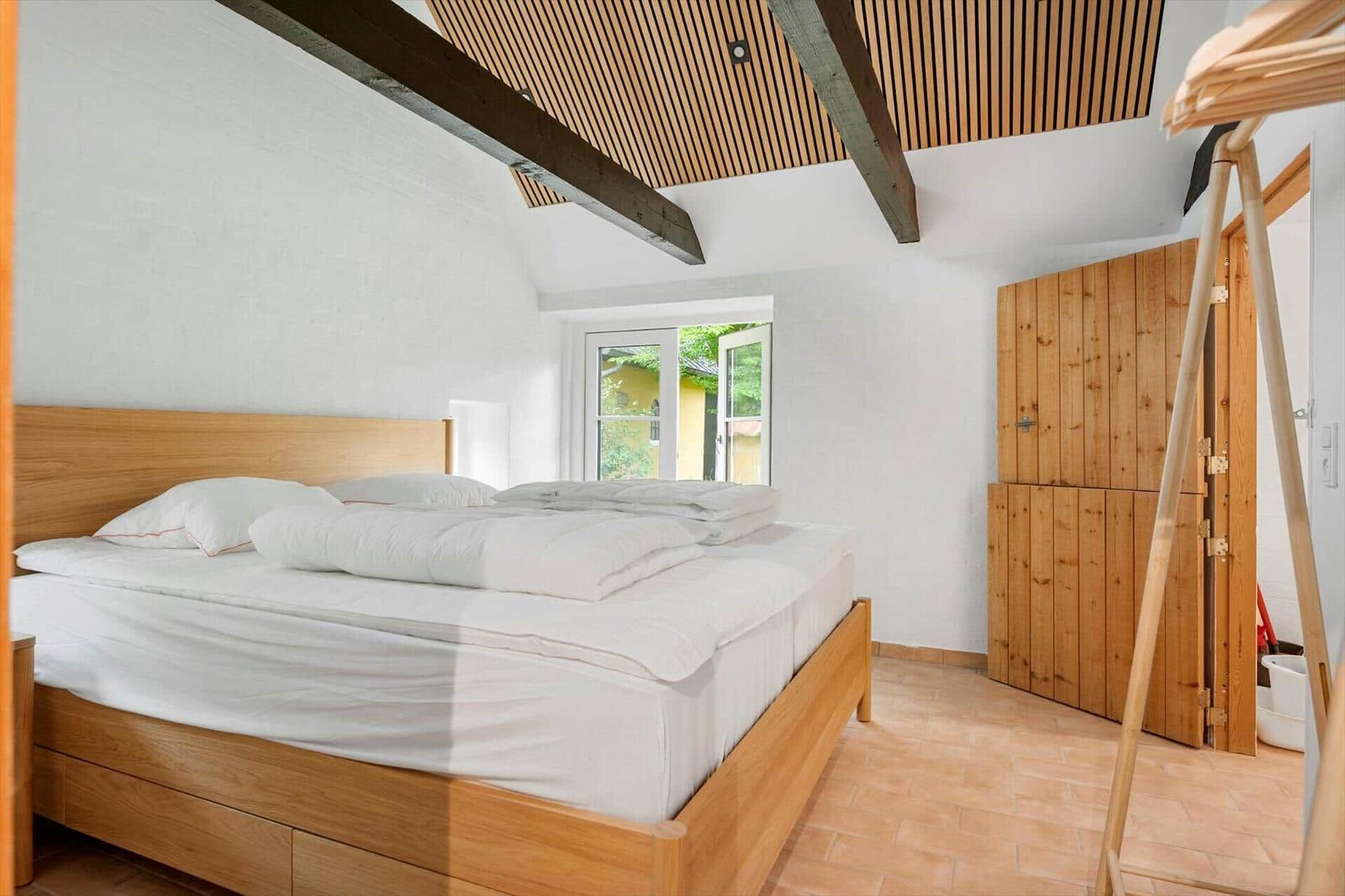 Bedroom with wooden bed, window and wooden wall. Wooden ceiling with beams.