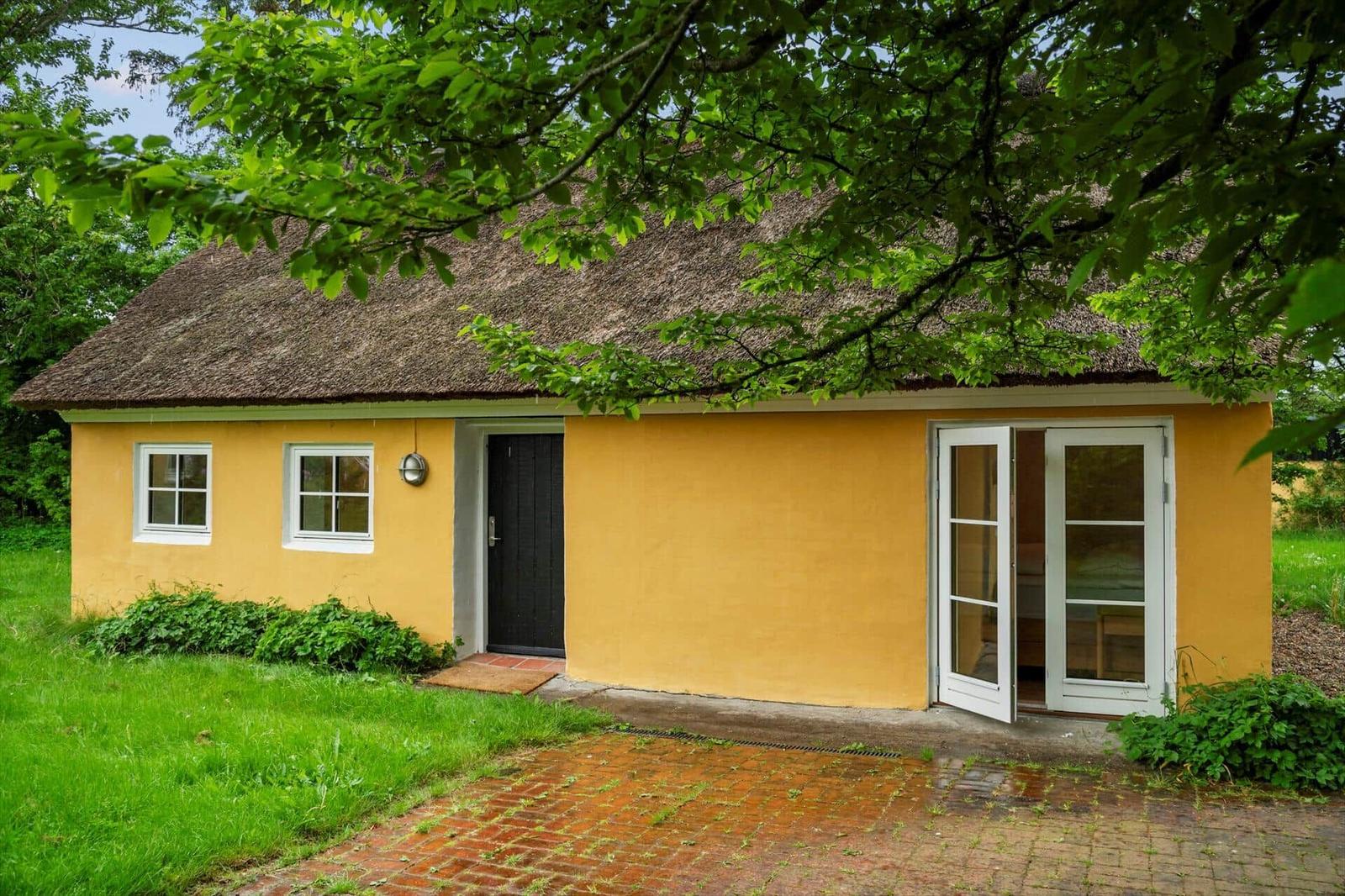A yellow house with a thatched roof, white windows, and a terrace.