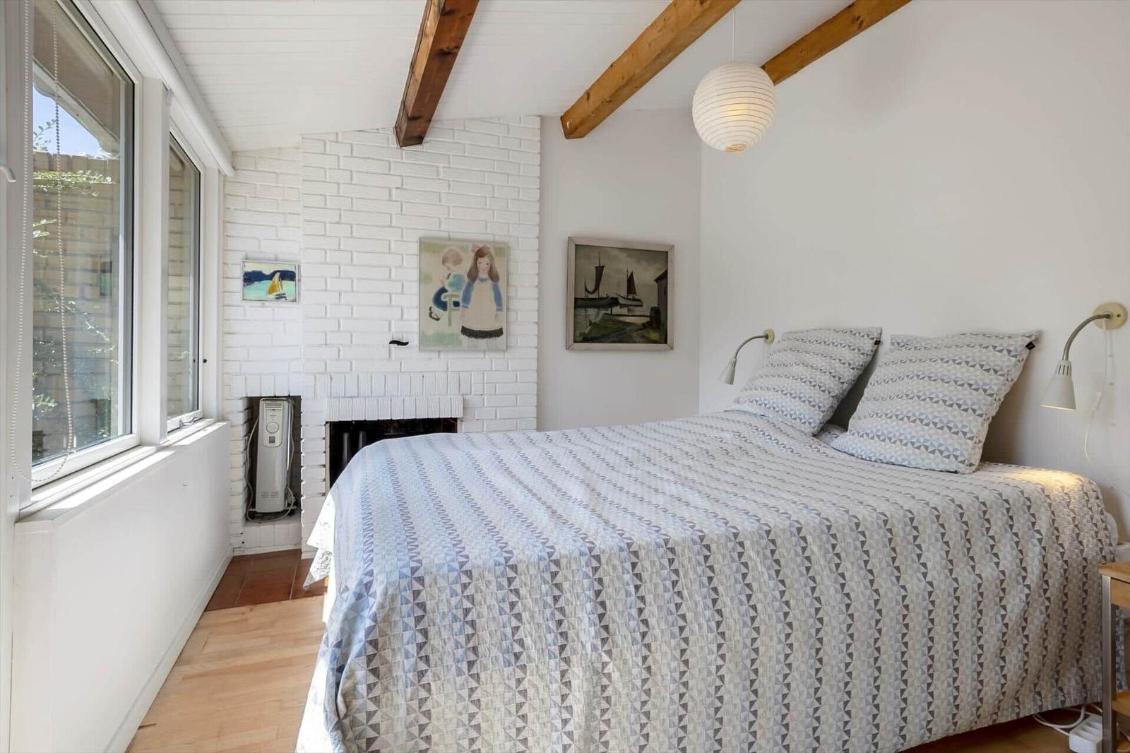 Bedroom with bed, window, fireplace, and ceiling beams.