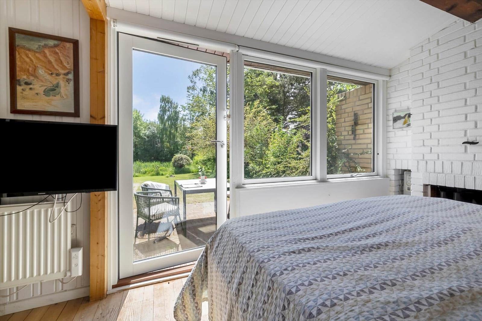 Bedroom with garden view. French doors and windows. Bed with patterned duvet.