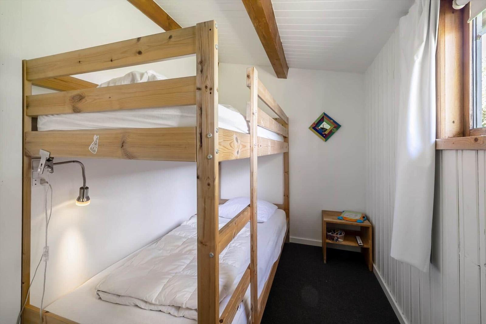 Room with wooden bunk bed, nightstand, and window with curtain.