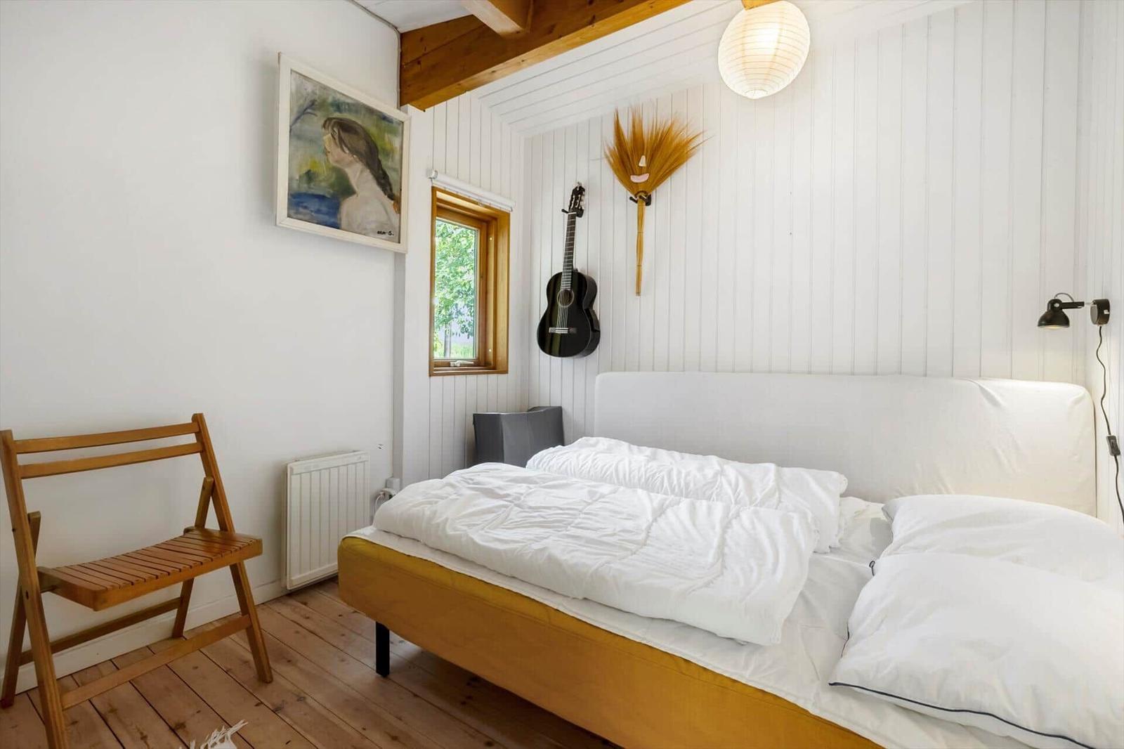 Bedroom with bed, chair, wall art, guitar, and window.