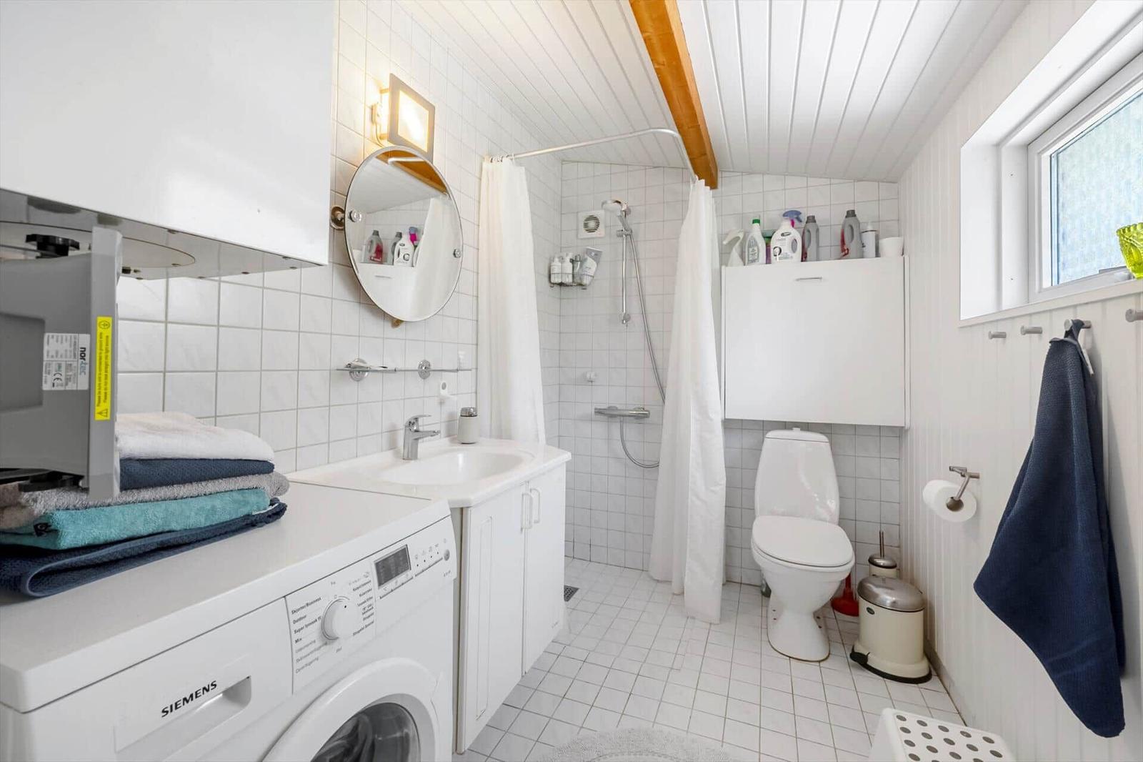 Bathroom with shower, toilet, and washing machine. White tiles and wooden beams.