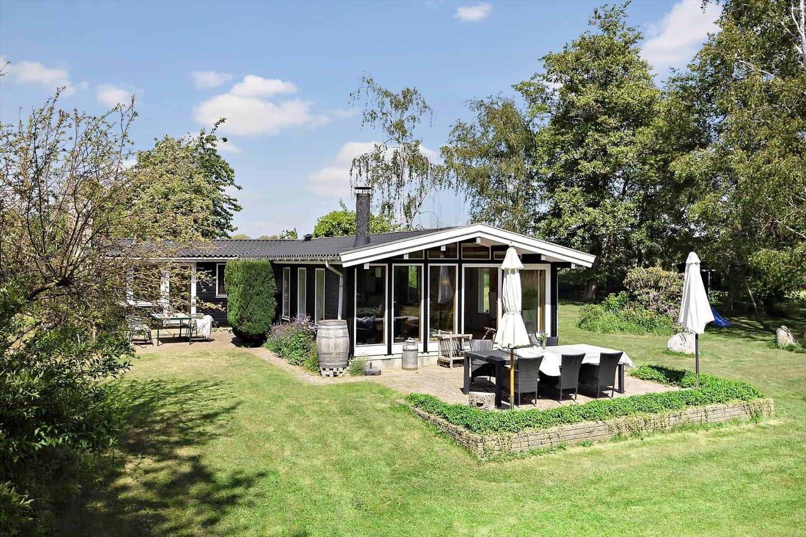 A house with terrace, garden and barbecue area. Surrounded by trees and grass.