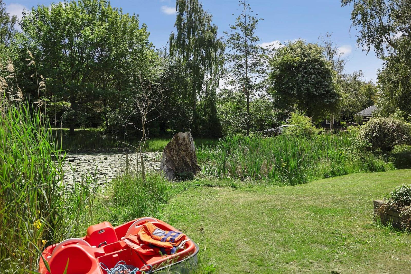 Red pedal boat by a pond with grass and trees in the background.