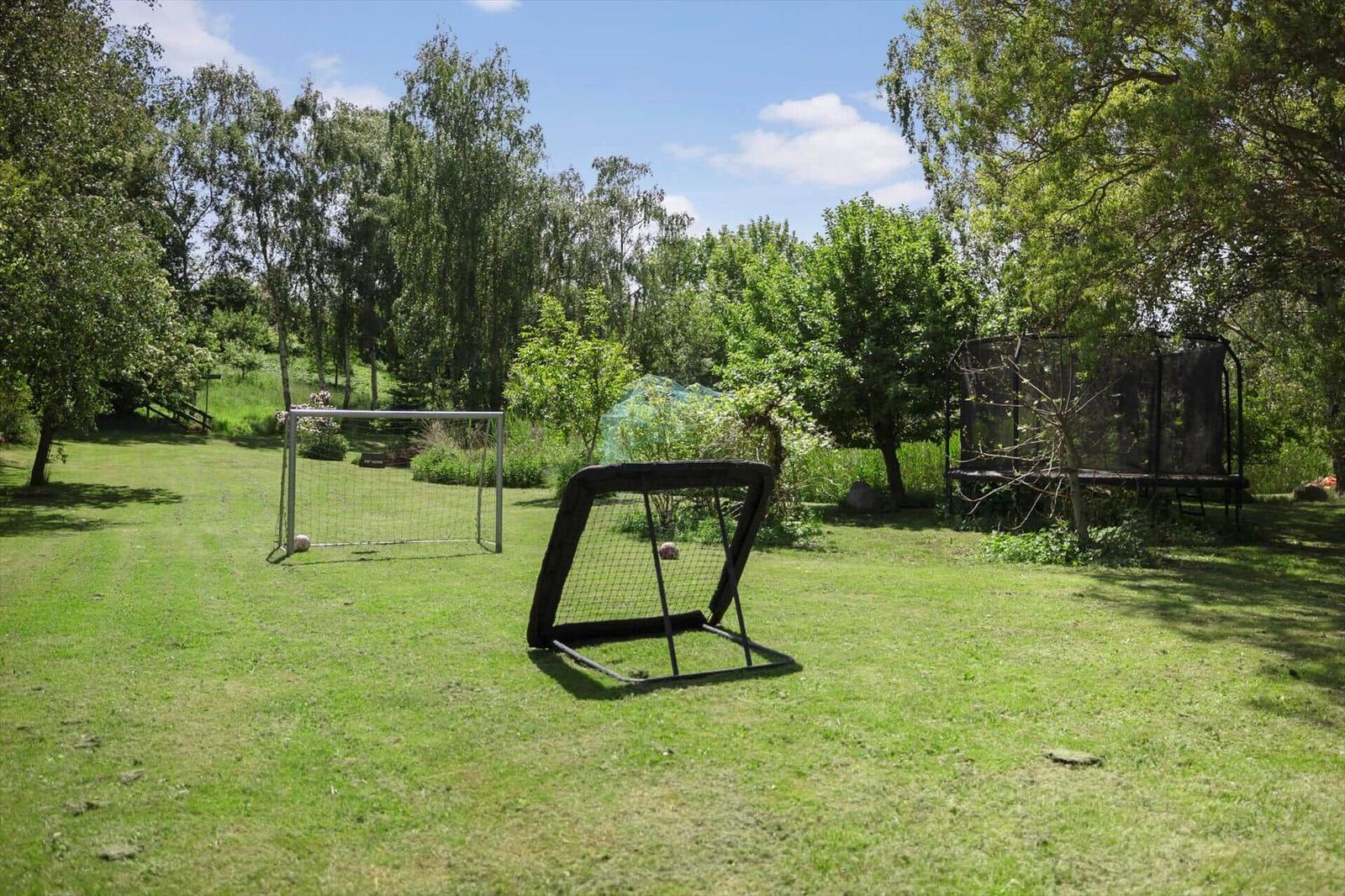 Green garden with soccer goal, training net, and trampoline under trees.