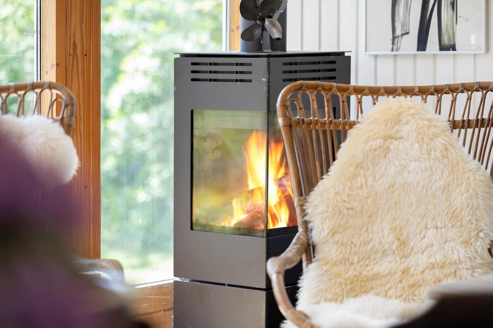 A wood-burning stove with fire between two chairs with fur throws.