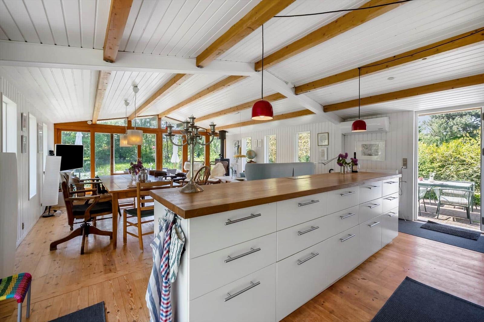 Kitchen with wooden countertop and white drawers. Wooden floor and beams on ceiling. View of garden.