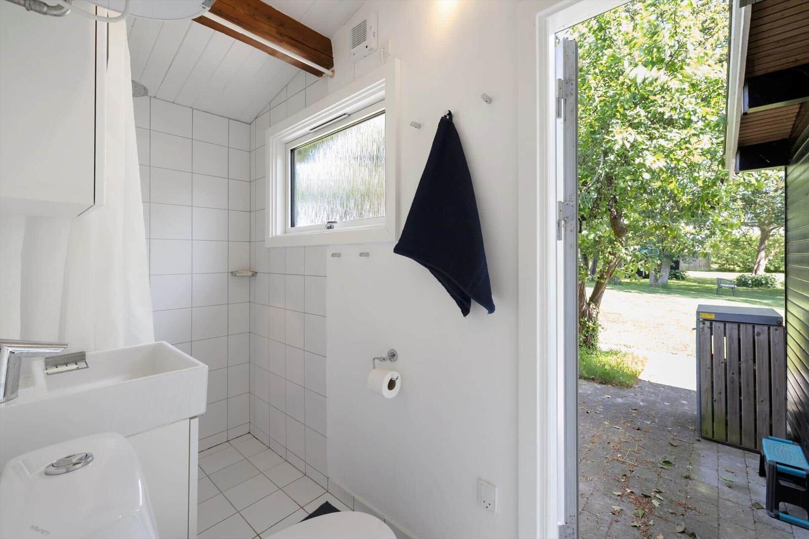 Bathroom with shower, sink, and toilet. Door leads to an outdoor area with trees.