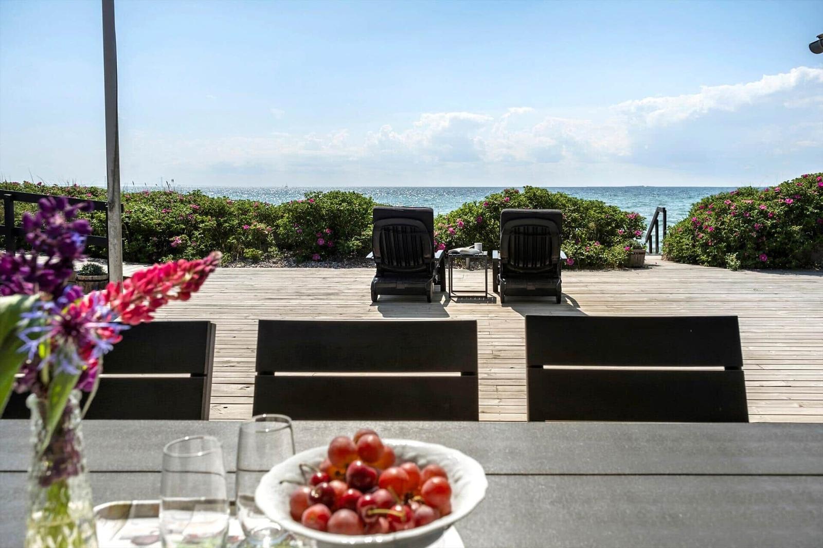 Terrasse mit Blick auf das Meer, zwei Liegestühle und Blumen im Vordergrund.