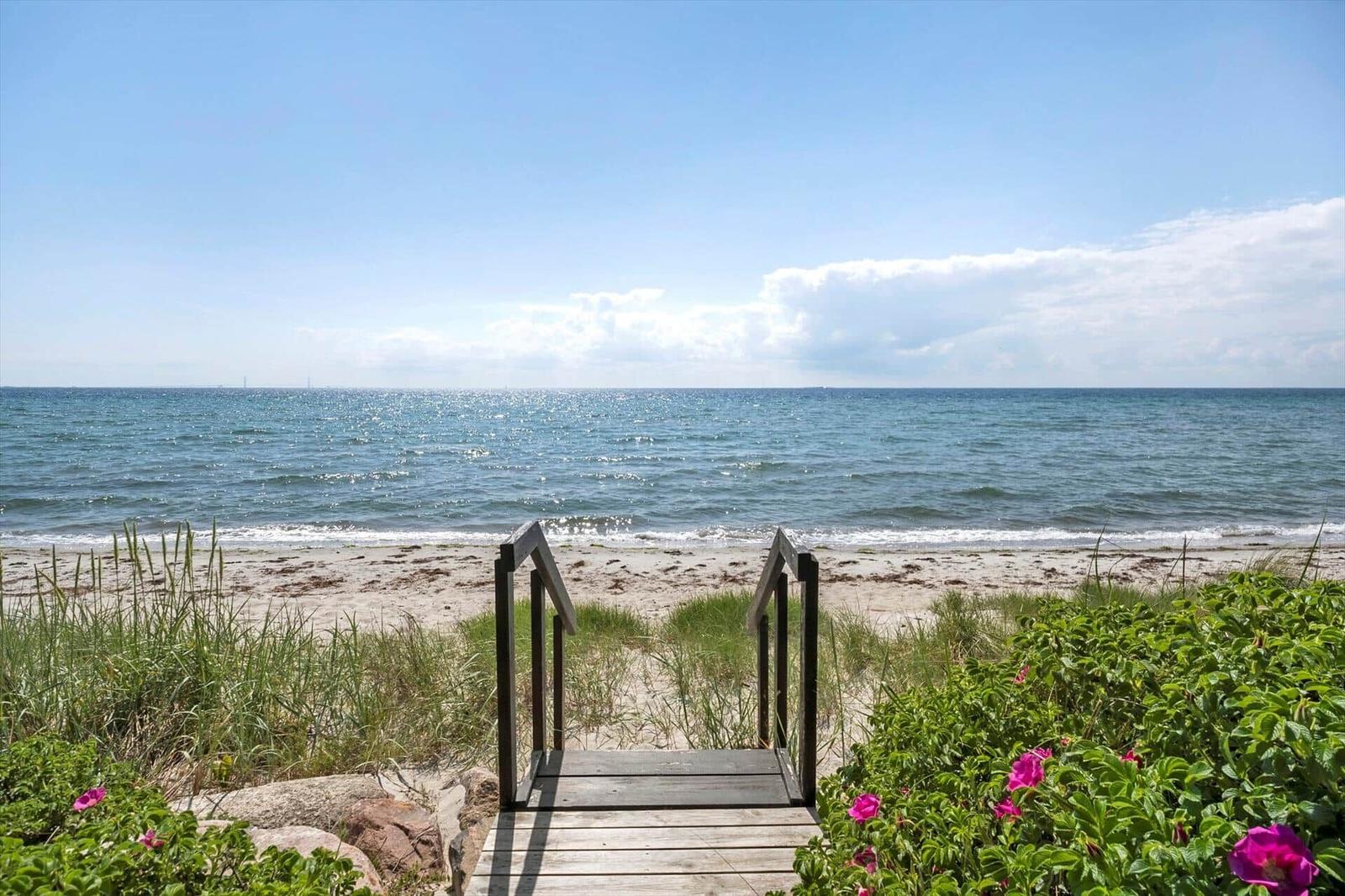 Holzsteg führt zum Strand. Blaues Meer und Himmel mit weißen Wolken.