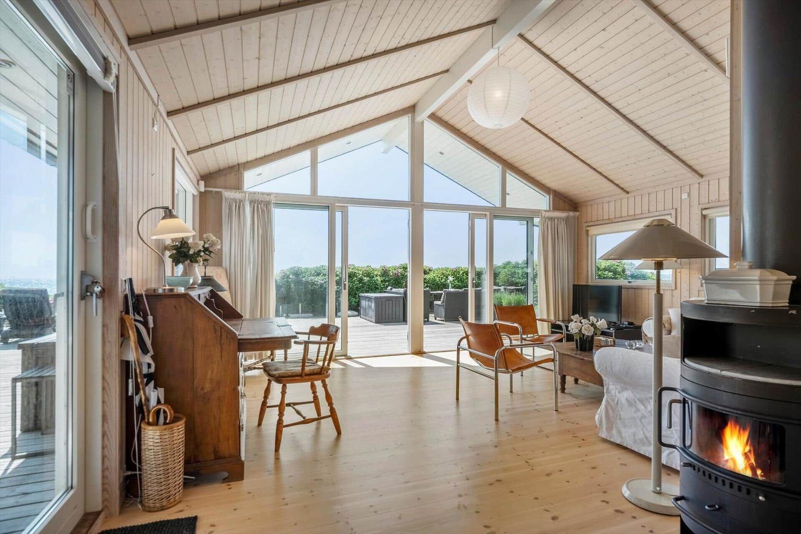 Wohnraum mit Holzdecke, Kamin und großem Fensterblick auf Terrasse