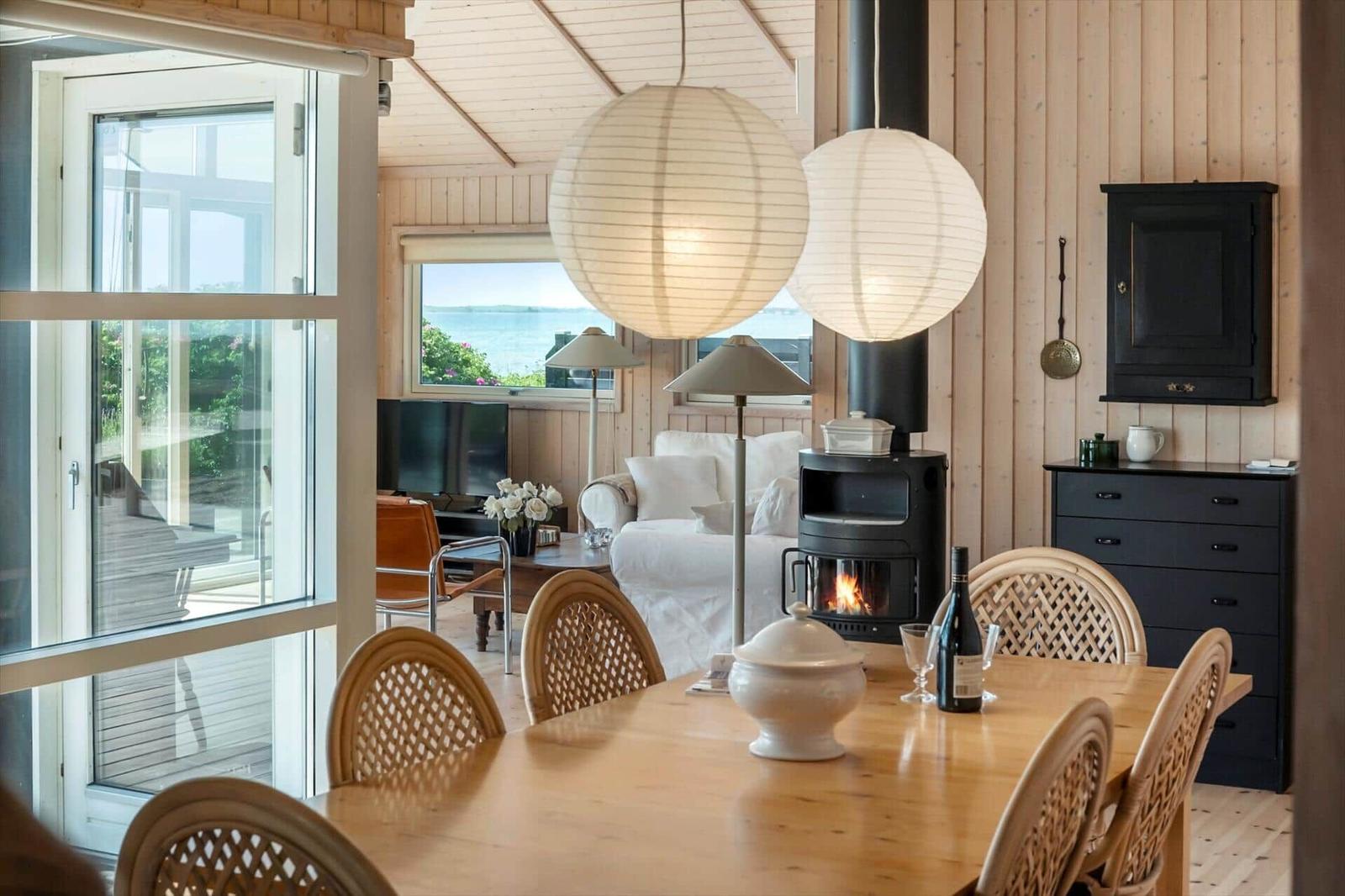 Ein Esszimmer mit Holztisch und Stühlen, Blick auf Wohnbereich mit Kamin und Meerblick.