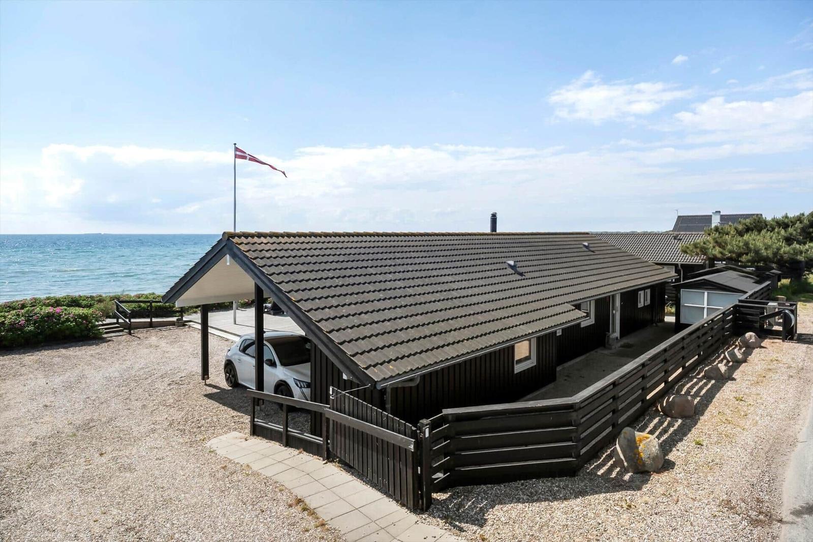 Holzhaus mit Dach, Fahne und Auto vor Meer