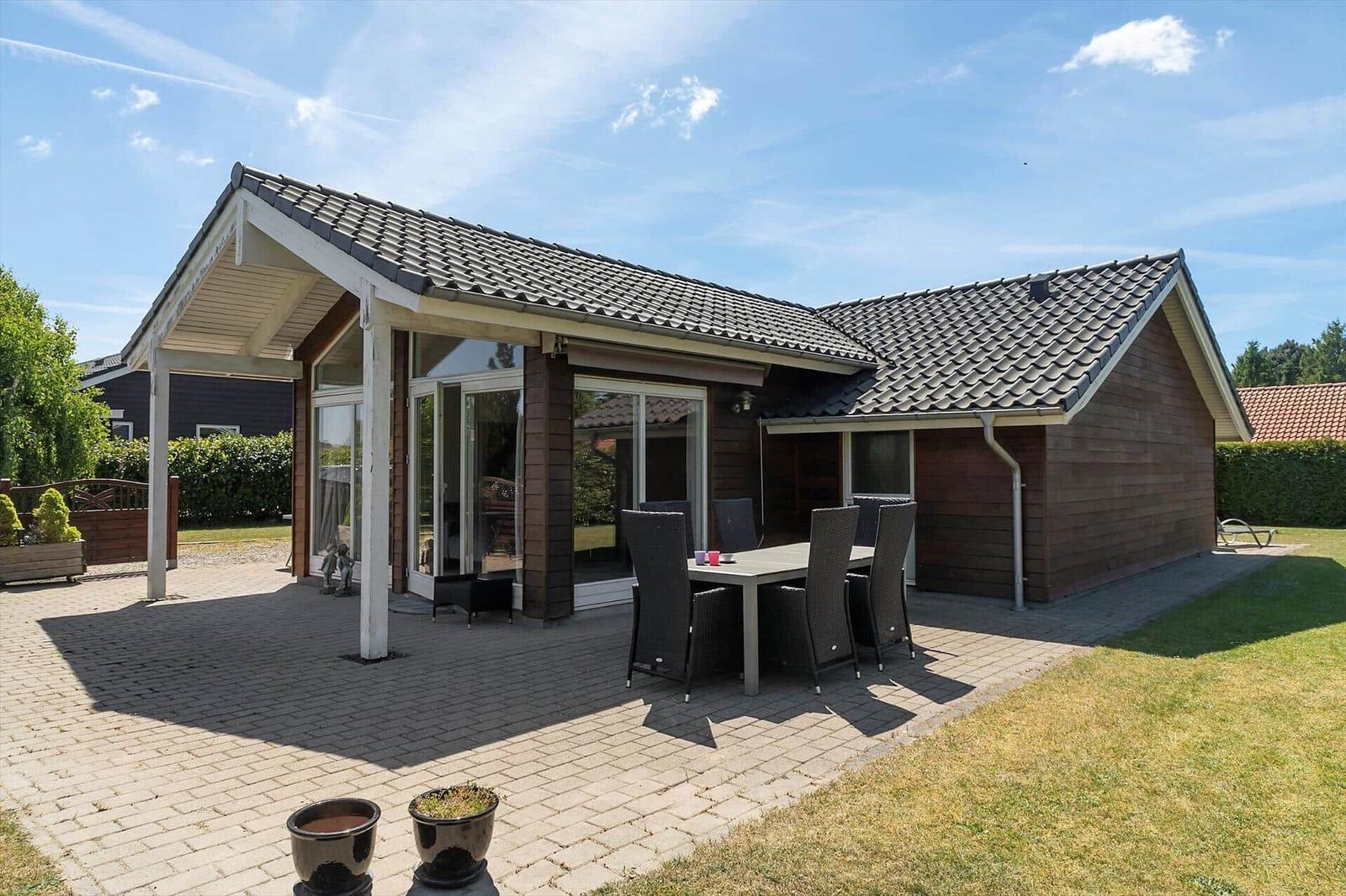 Moderne Ferienwohnung mit Terrasse, Sitzgruppe und Garten. Gepflasterte Fläche und Holzfassade.