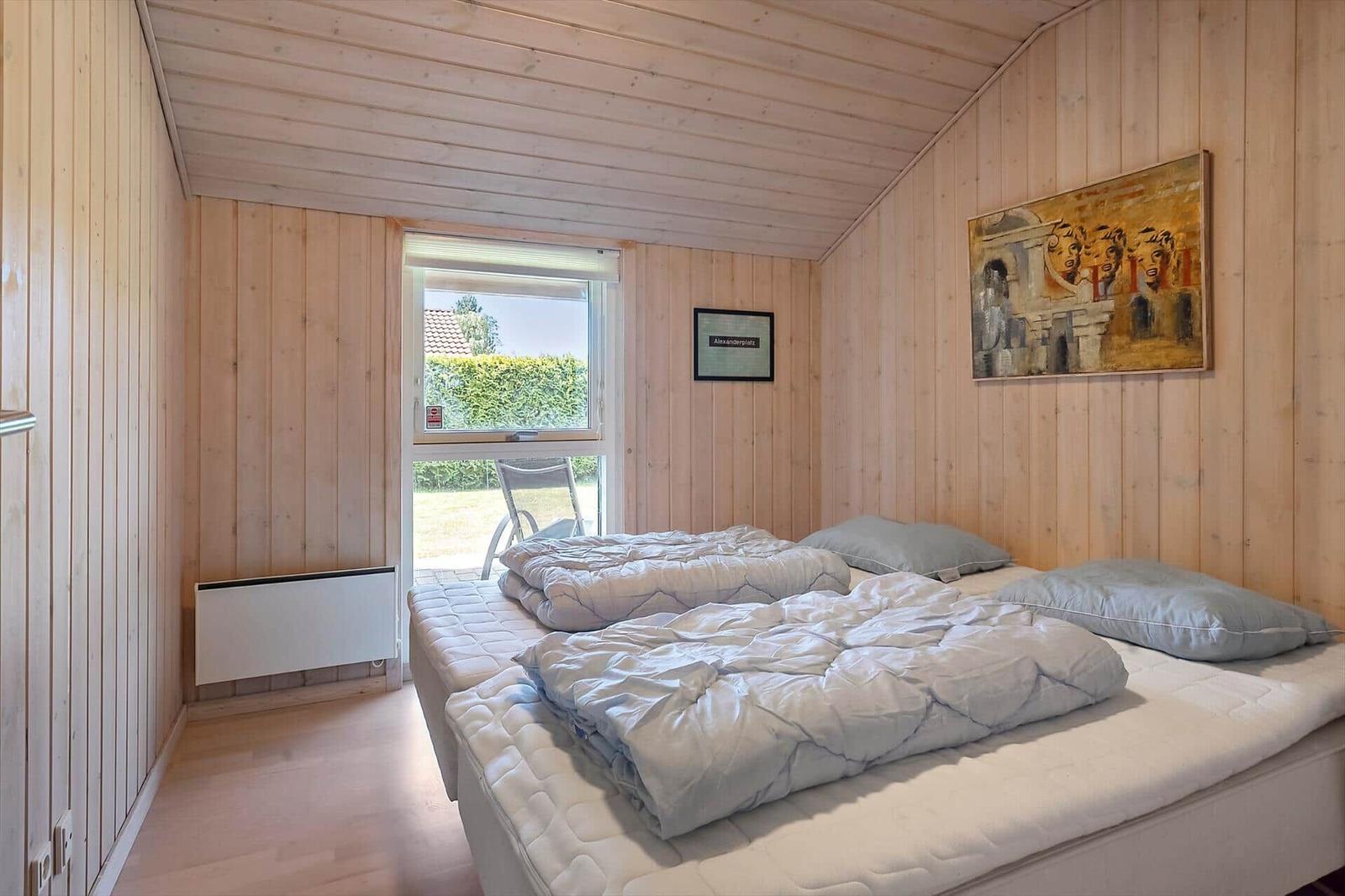 Schlafzimmer mit Holzwand, Bett und Fenster zur Außenterrasse.