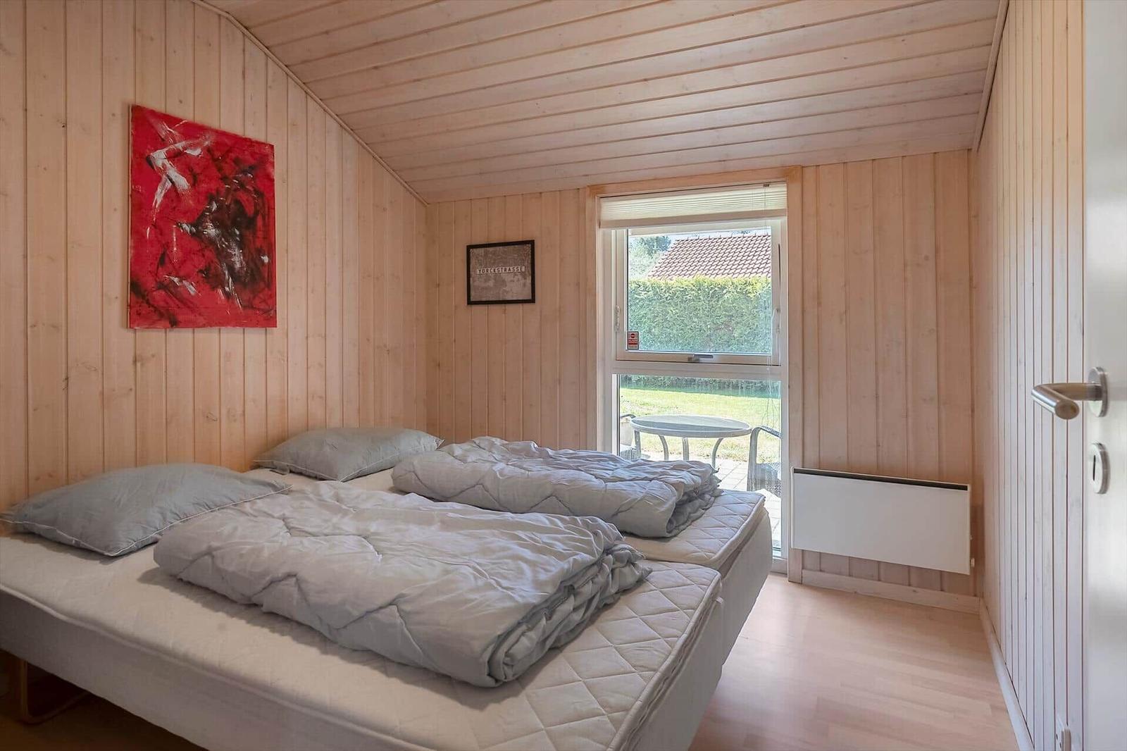 Schlafzimmer mit Holzwand, Bett, Fenster und Wandbild.