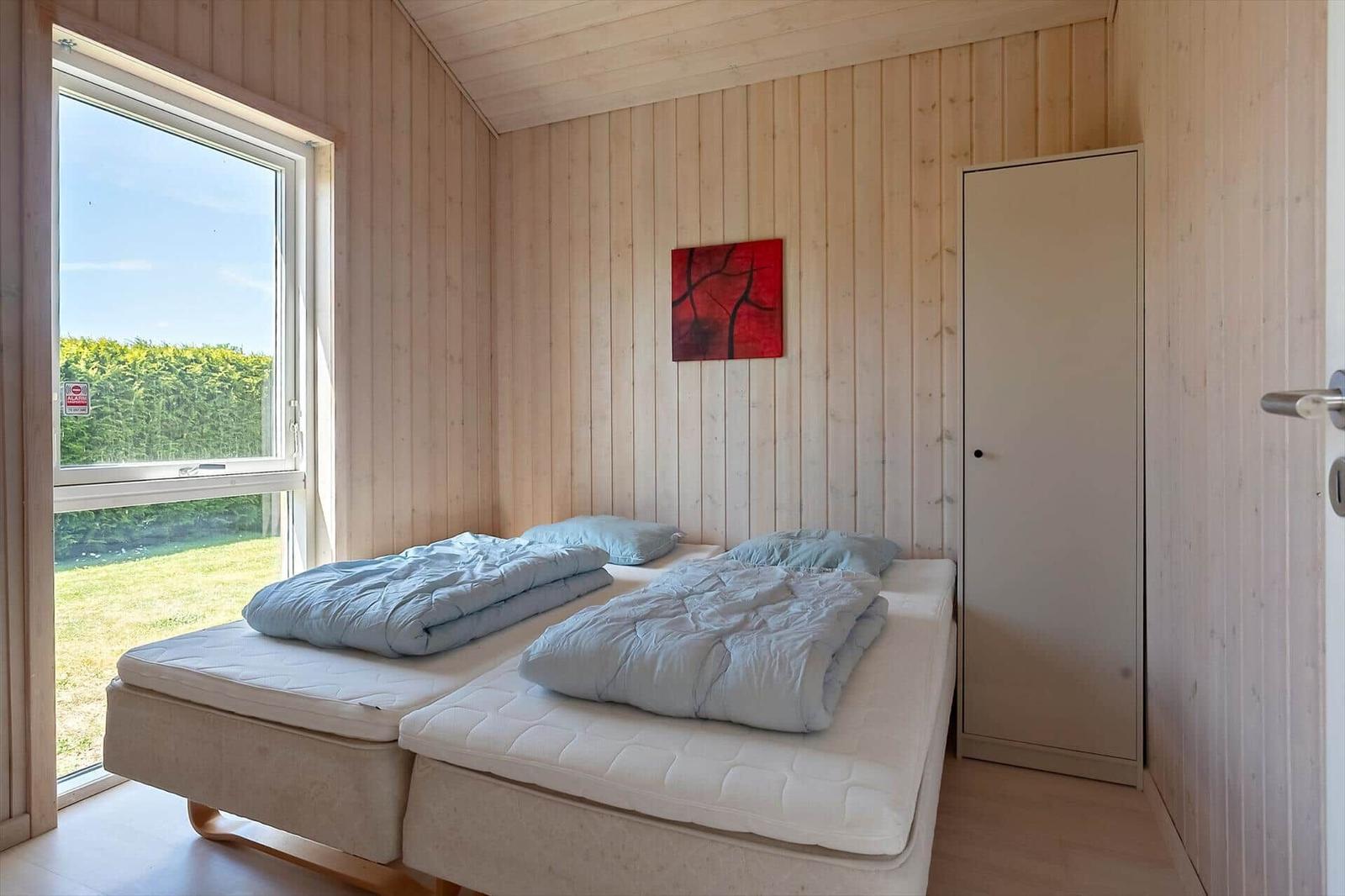 Zimmer mit zwei Matratzen, Holzwand und Fenster mit Blick auf Grünfläche.