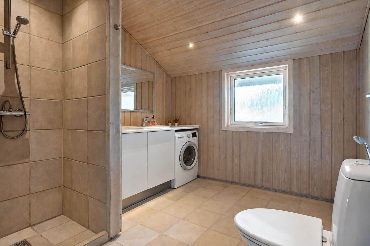 Badezimmer mit Dusche, Waschmaschine und Toilette. Holzwand und -decke.
