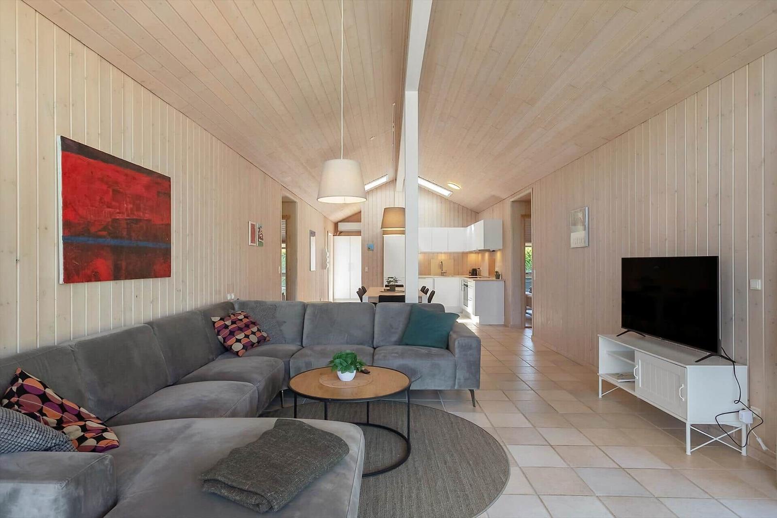 Wohnbereich mit Sofa, TV und Küchenbereich. Holzwände und Bodenfliesen.