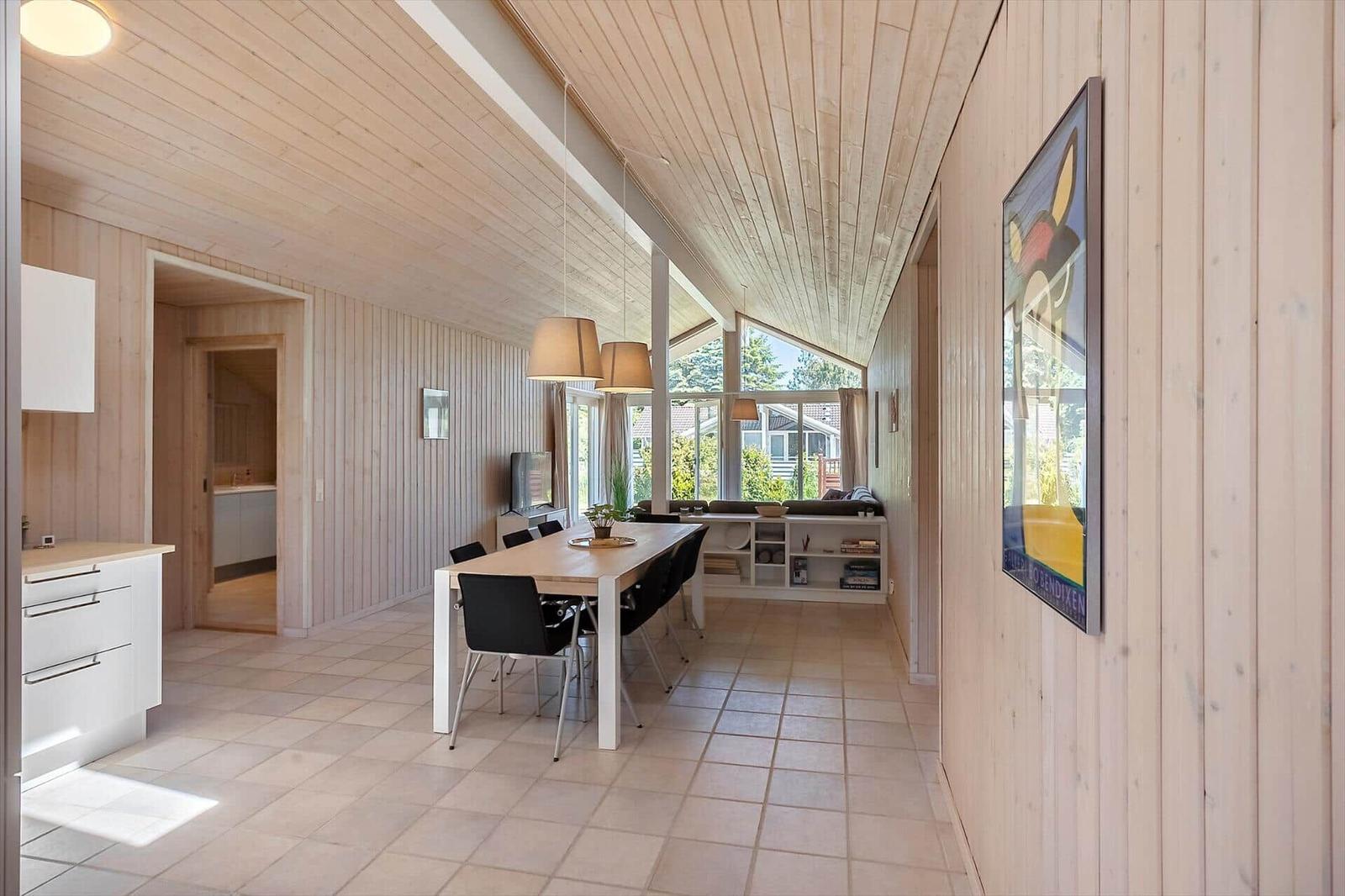 Langgestreckter Raum mit Essbereich, Küchenzeile und großem Fenster. Holzwände und -decke.
