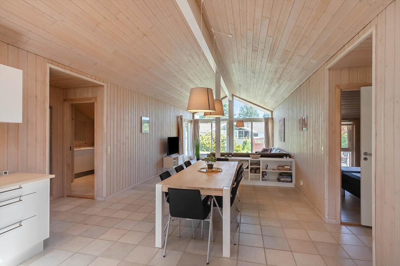 Langgestreckter Raum mit Essbereich, Wohnbereich und Blick auf Garten. Holzwände und -decke.