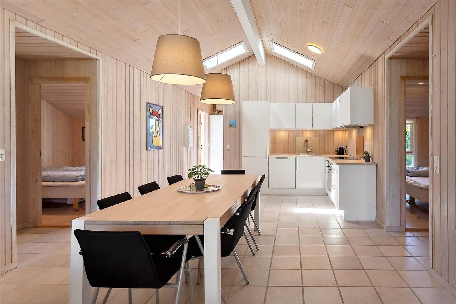 Essbereich mit Tisch und Stühlen, Küche und Schlafzimmer im Hintergrund.