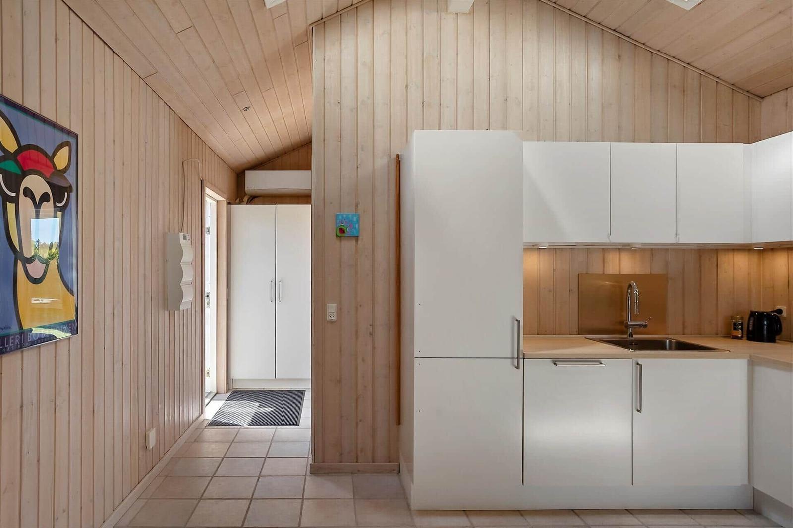 Küche mit weißen Schränken und Holzwänden. Flur mit Tür und Wandbild.