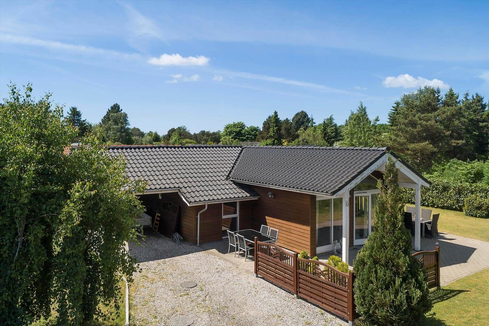 Ein Haus mit Holzfassade, Terrasse und Garten. Hintergrund: Bäume und blauer Himmel.