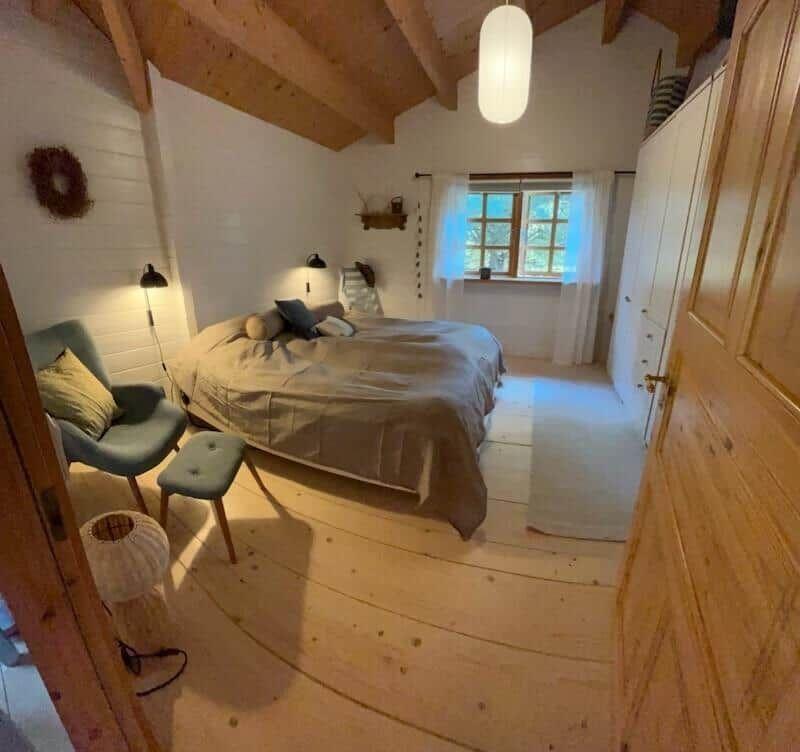 Schlafzimmer mit Bett, Stuhl und Fenster. Holzdecke und -boden.