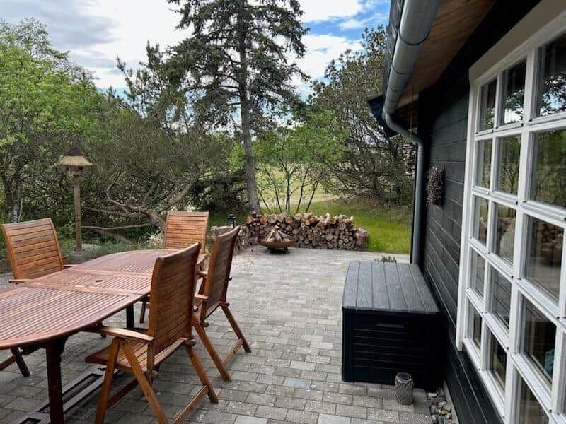Terrasse mit Holztisch, Stühlen und Holzstapel im Hintergrund.