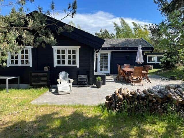 Schwarze Hütte mit weiß gerahmten Fenstern und Terrasse mit Holztisch und Stühlen.