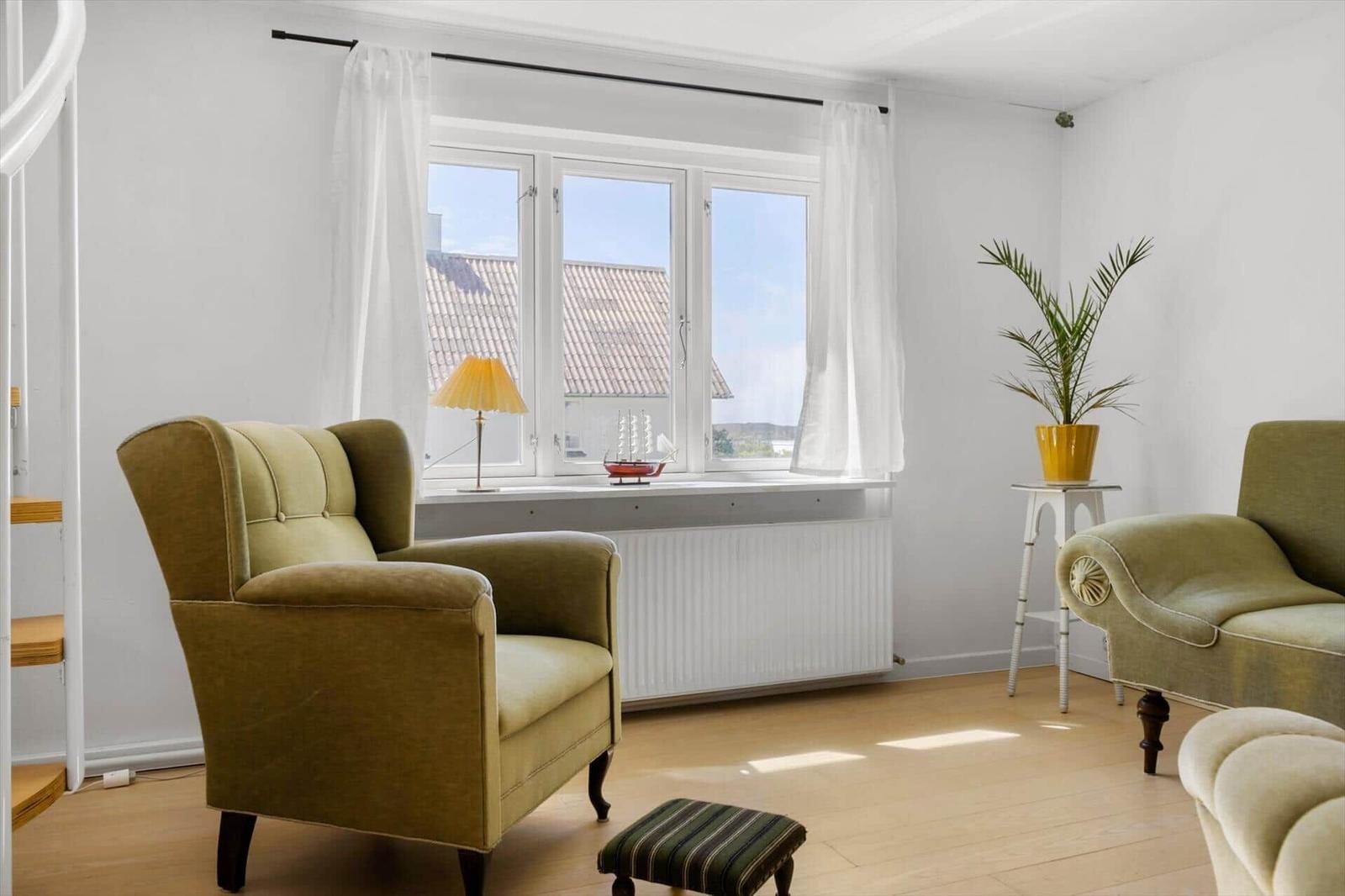 Ein Raum mit zwei grünen Sesseln, einem Fenster und einer Pflanze auf einem Tisch.