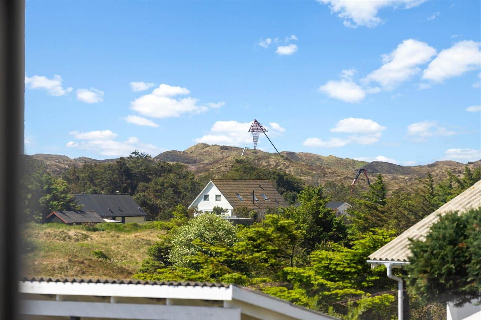 Weitläufiger Blick auf Hügel mit Windkraftanlage und Häusern unter blauem Himmel.