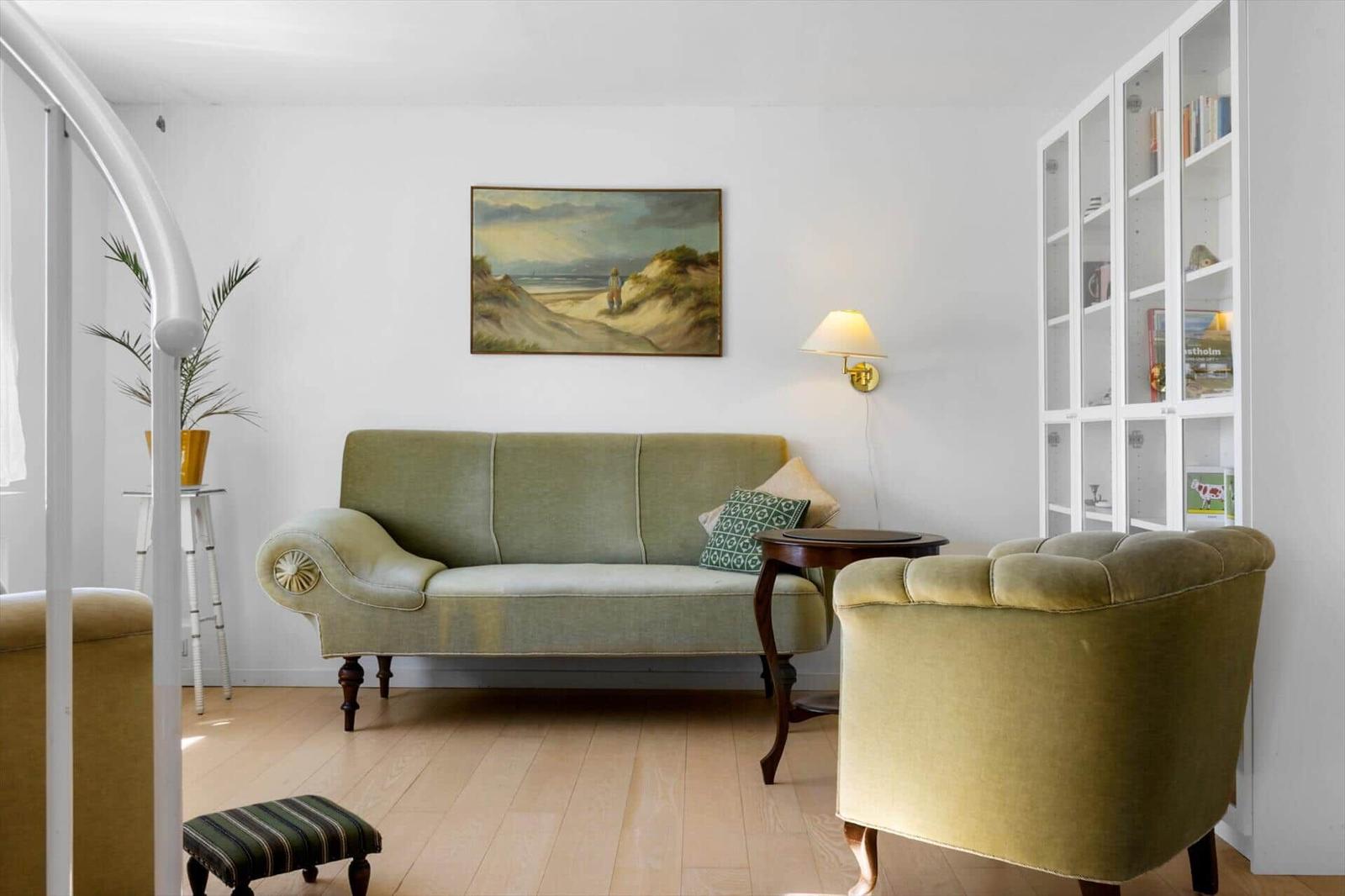 Ein Wohnzimmer mit grünem Sofa, Sessel und Bücherregal an der Wand.