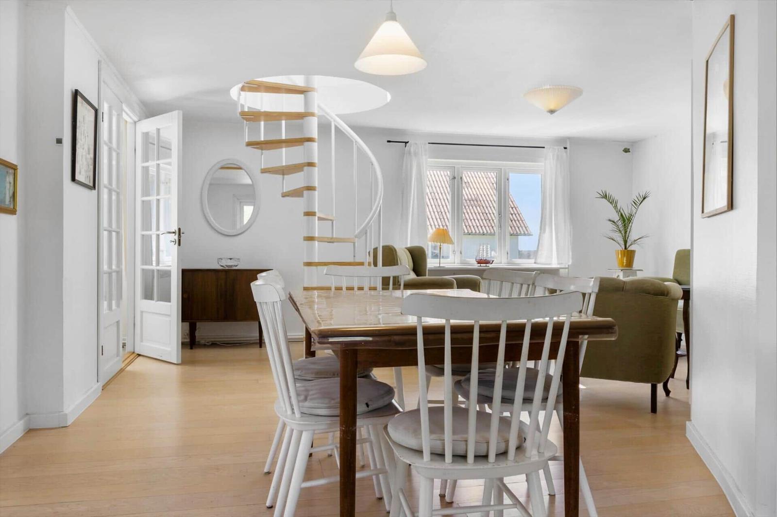 Esszimmer mit Tisch, Stühlen und Blick auf Wohnzimmer mit Wendeltreppe.