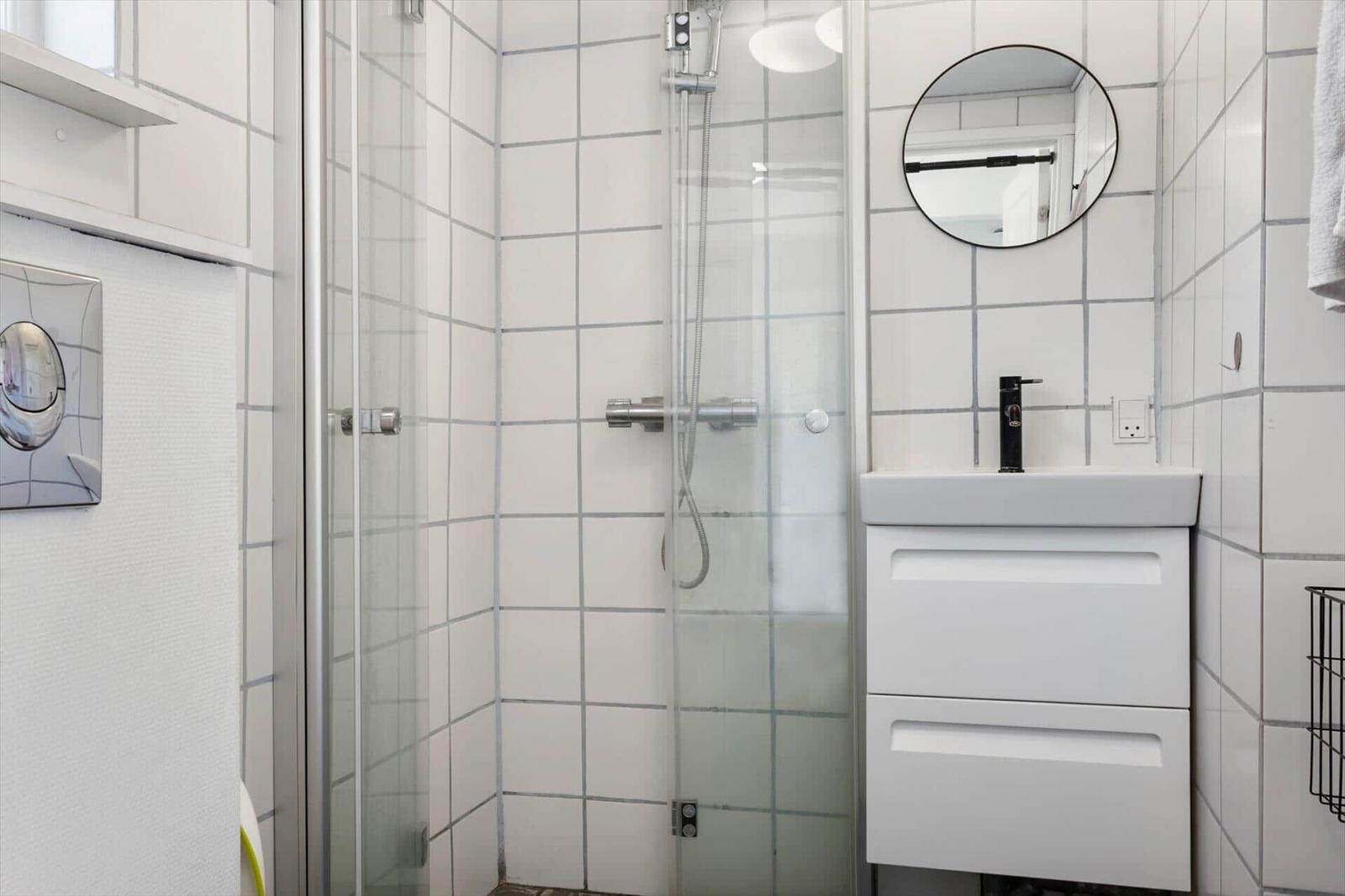 Dusche mit Glaswand, Waschbecken und Spiegel an der Wand.