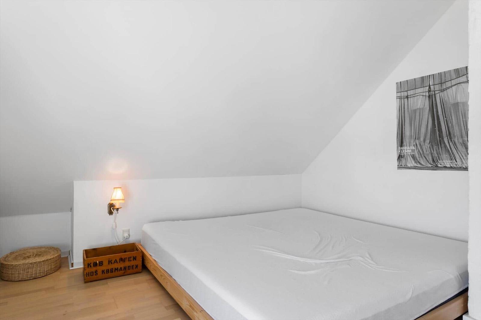 Schlafzimmer mit Dachschrägen, Bett, Wandlampe und Poster an der Wand.