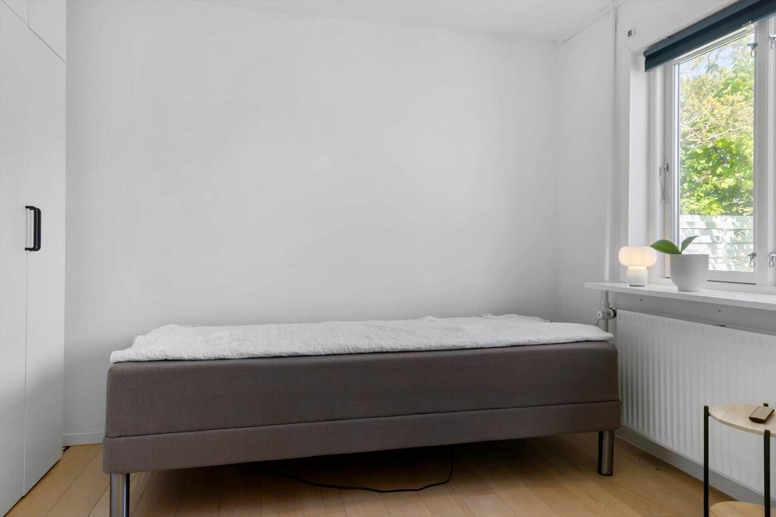 Ein Schlafzimmer mit Bett, Fenster und Schrank. Die Wand ist weiß.