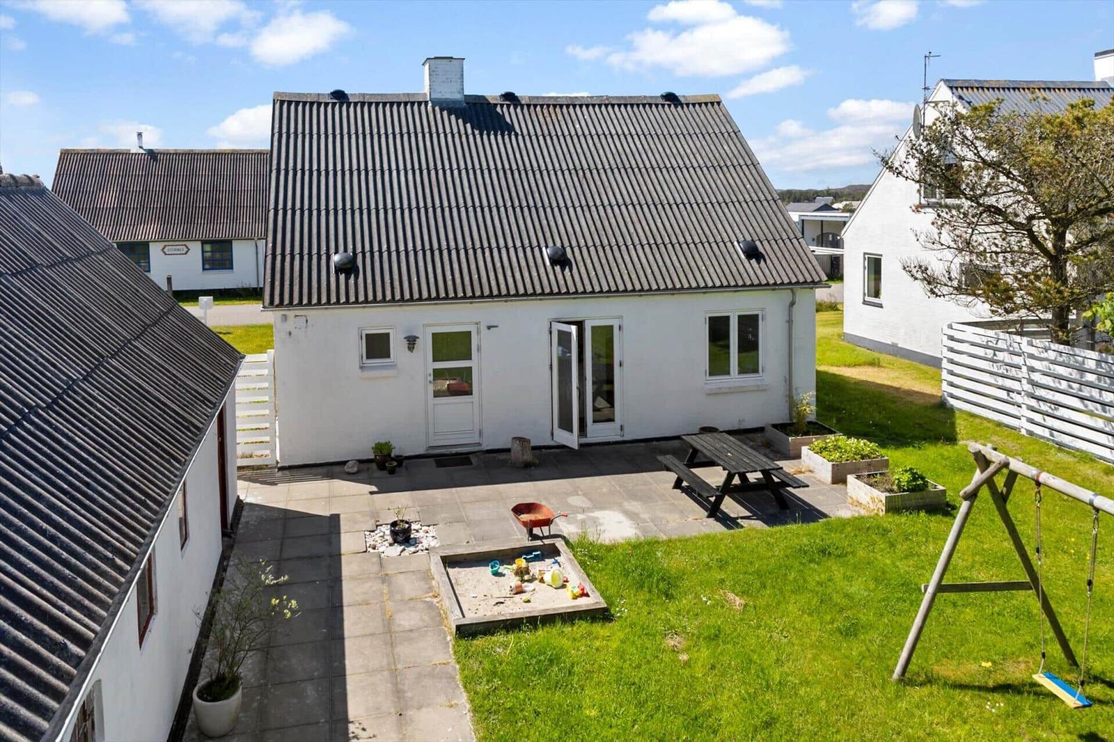 Ein weißes Haus mit dunklem Dach, Garten, Picknicktisch und Schaukel.