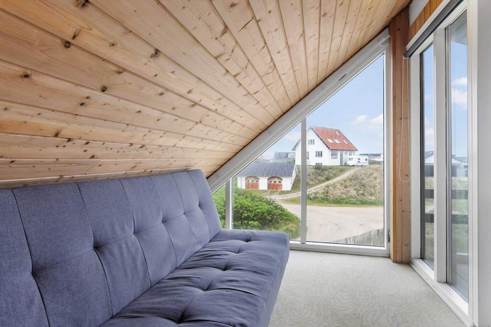 Ein grauer Sofa unter einer Holzdecke mit Blick auf eine Straße und Häuser.