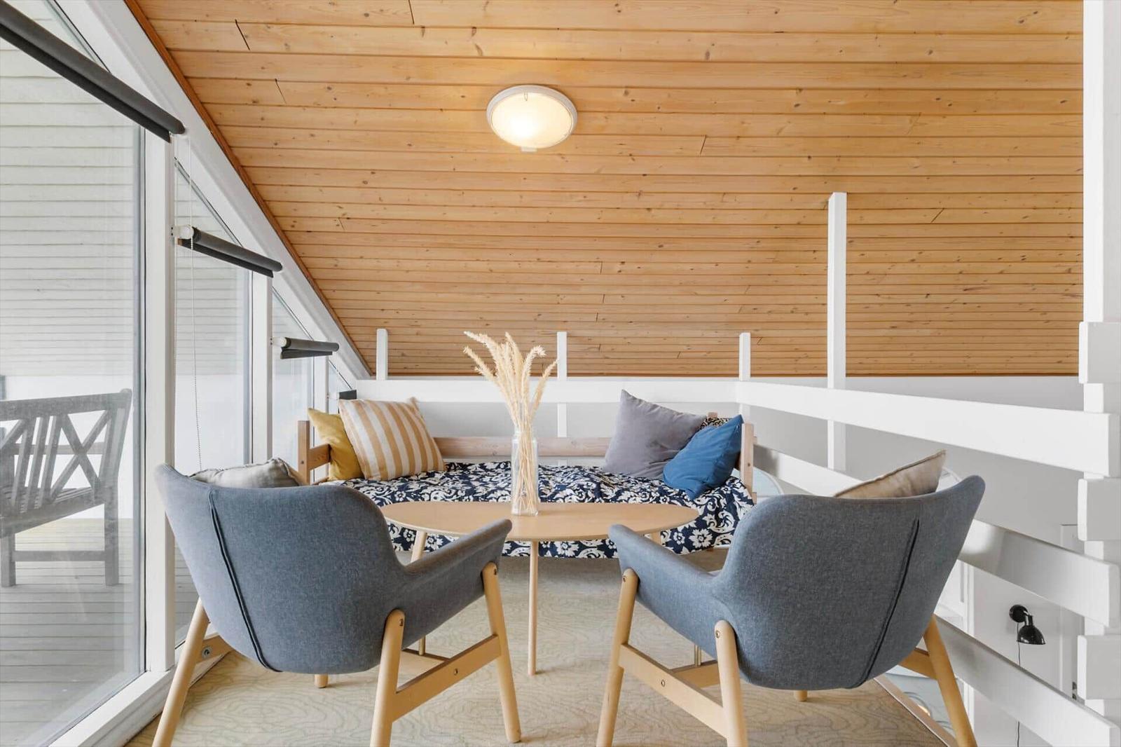 Zimmer mit Holzdecke, zwei grauen Stühlen und einem Sofa mit Kissen.