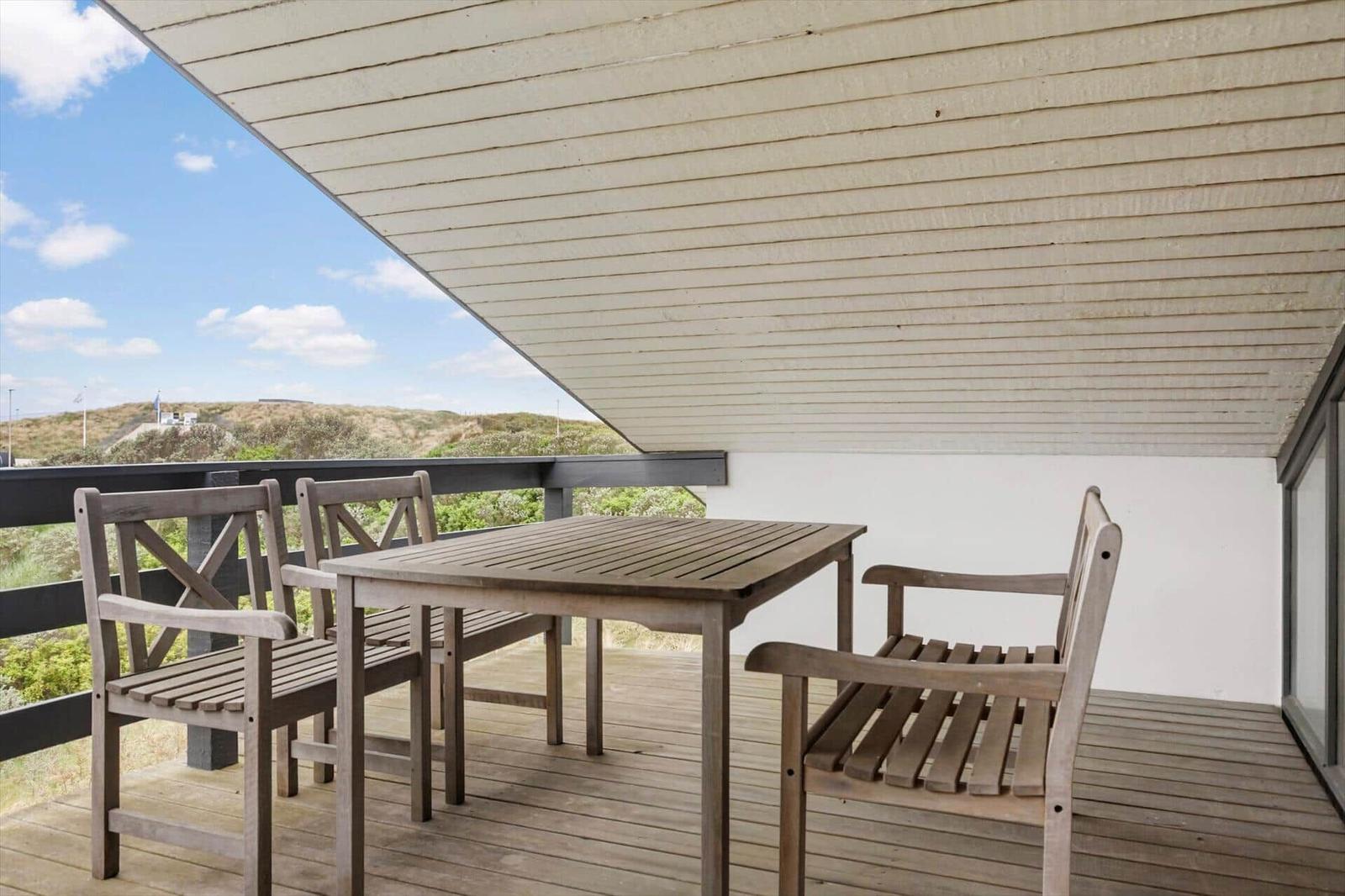 Terrasse mit Tisch und Stühlen, Blick auf Dünen und Himmel.