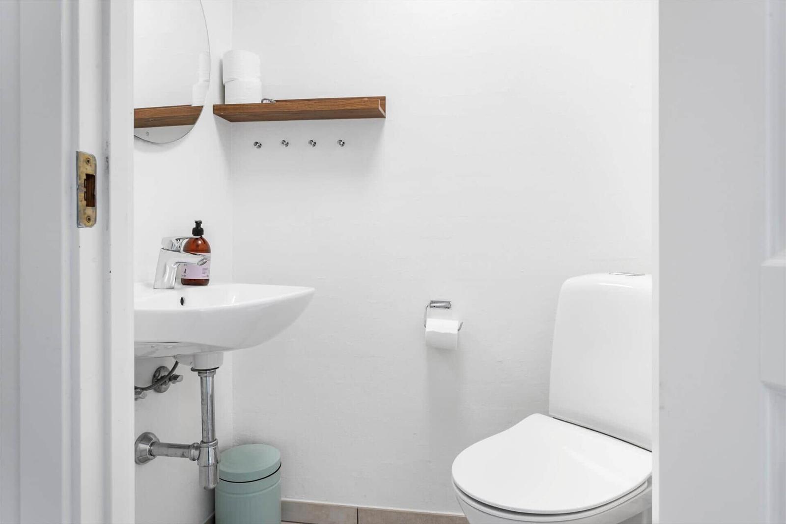 Badezimmer mit Toilette, Waschbecken und Holzregal an der Wand.