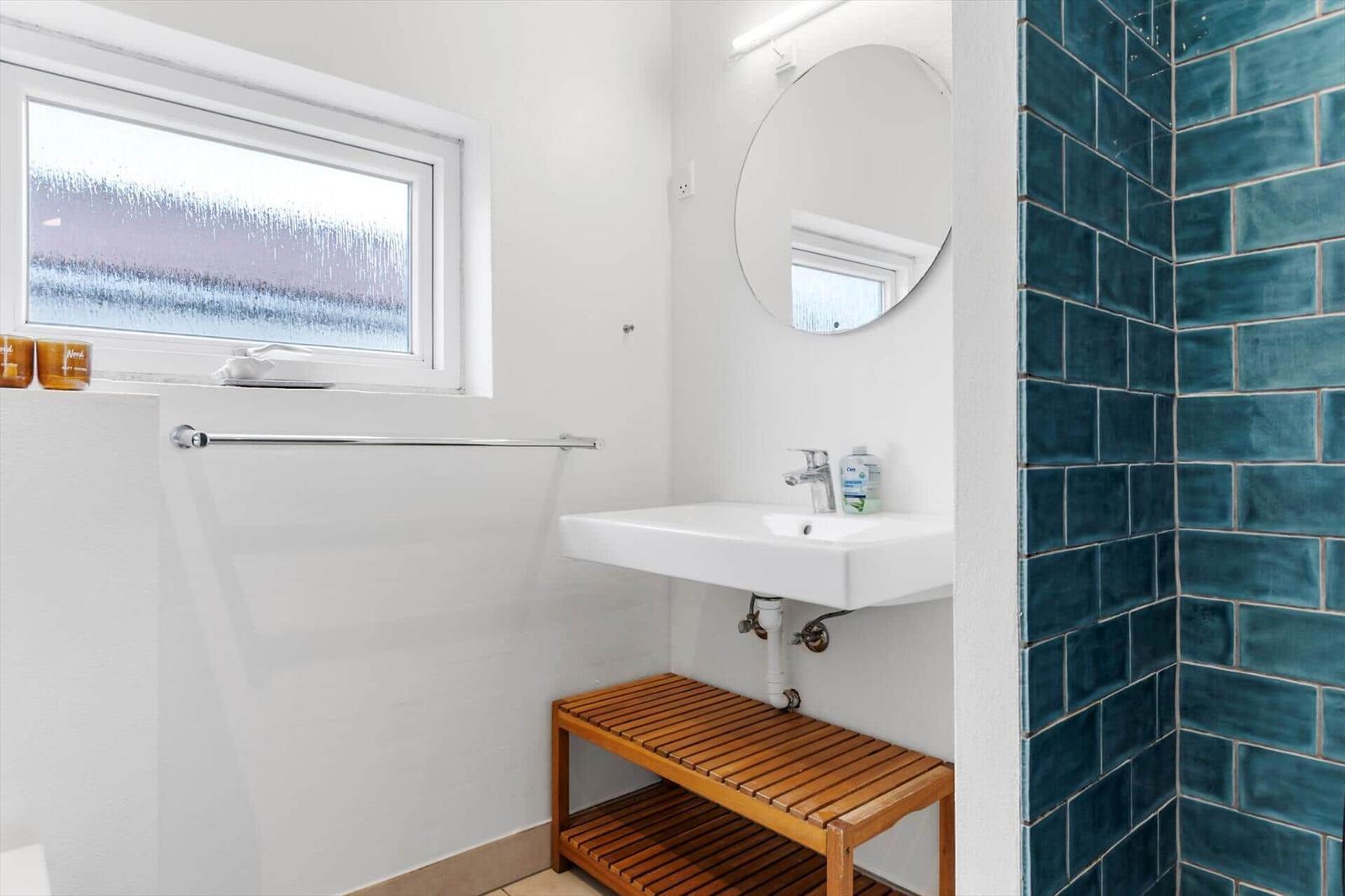 Badezimmer mit Waschbecken, Spiegel, Fenster und blauen Fliesen.