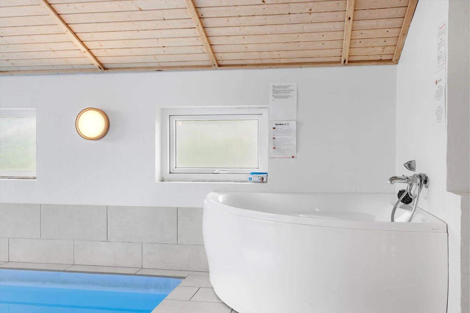 Bad mit Whirlpool, Dusche und Fenster. Holzdecke und weiße Wände.